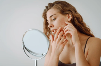 Femme examinant sa peau dans un miroir, représentant une réflexion sur les soins de la peau et la gestion des imperfections.