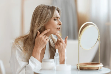 Femme examinant sa peau dans un miroir, symbolisant l’importance d’une routine de soins pour traiter et prévenir l’acné.