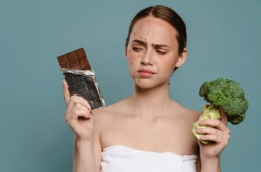 Femme tenant une barre de chocolat et du brocoli, illustrant le lien entre alimentation et santé de la peau, en particulier l’impact sur l’acné adulte.